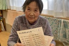 入居者が手書きの文字作品を持って笑顔で写っている風景